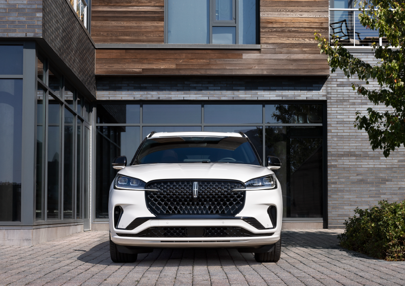 A white 2025 Lincoln Aviator® SUV is shown parked outside a modern building with gray brick and wood accents. | Planet Lincoln Love Field in Dallas TX