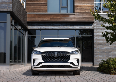 A white 2025 Lincoln Aviator® SUV is shown parked outside a modern building with gray brick and wood accents. | Planet Lincoln Love Field in Dallas TX