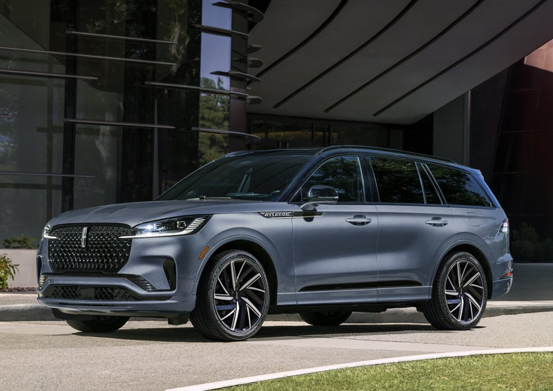 A gray 2025 Lincoln Aviator® SUV is parked outside a modern building showcasing the driver’s side of the vehicle. | Planet Lincoln Love Field in Dallas TX
