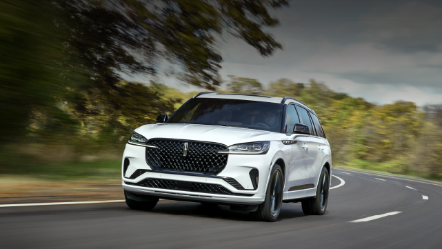 A white 2025 Lincoln Aviator® SUV is being driven down a road lined with trees. | Planet Lincoln Love Field in Dallas TX