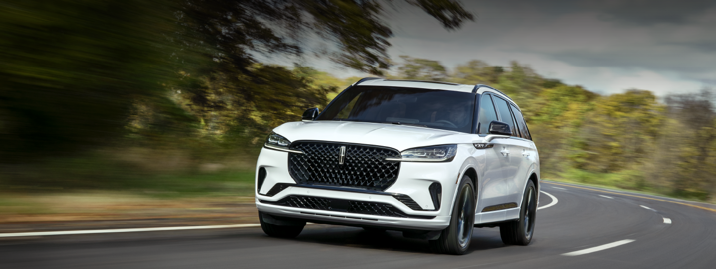 A white 2025 Lincoln Aviator® SUV is being driven down a road lined with trees. | Planet Lincoln Love Field in Dallas TX