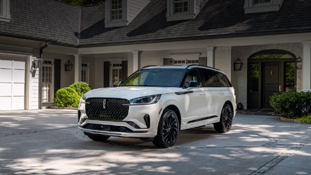 A white 2026 Lincoln Aviator® SUV is parked in the driveway of a luxury home. | Planet Lincoln Love Field in Dallas TX