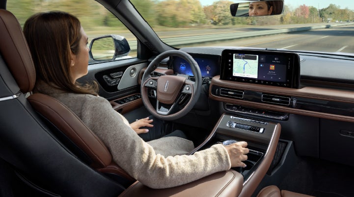 A 2027 Lincoln Aviator® SUV is being driven hands-free on a highway lined with trees. | Planet Lincoln Love Field in Dallas TX