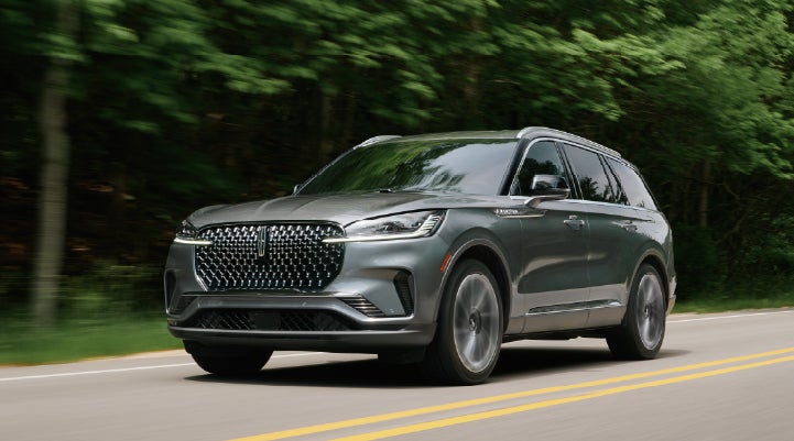A 2027 Lincoln Aviator® SUV is being driven down a road lined with trees. | Planet Lincoln Love Field in Dallas TX