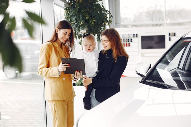 A friendly discussion between a car consultant and a customer with a child in a dealership setting